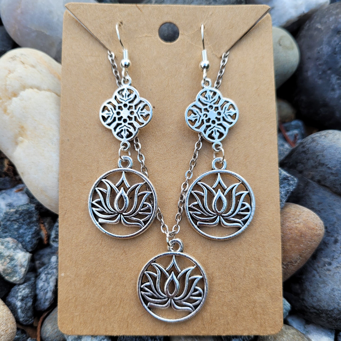Silver lotus flower earrings on a brown card with pebbles in the background