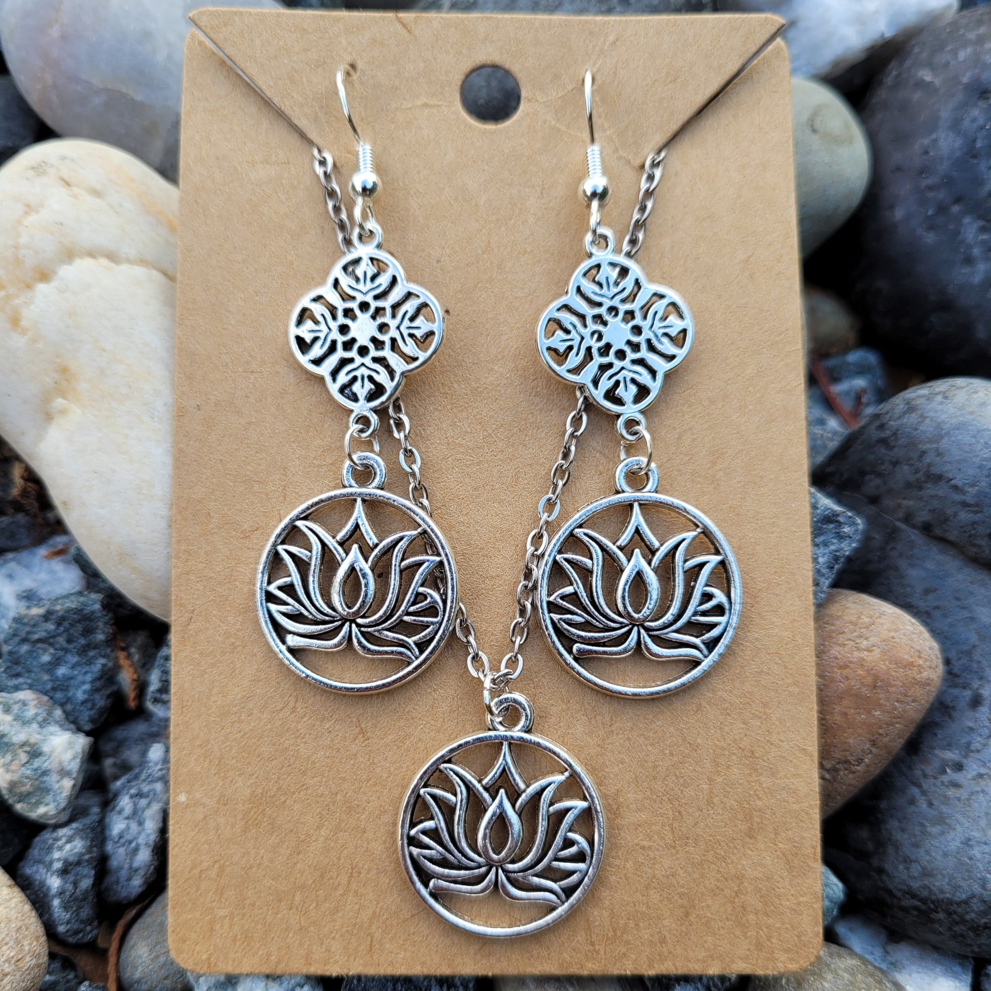 Silver lotus flower earrings on a brown card with pebbles in the background