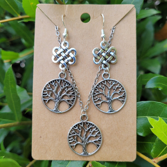 Silver tree-of-life earrings on a cardboard backing with green leaves in the background